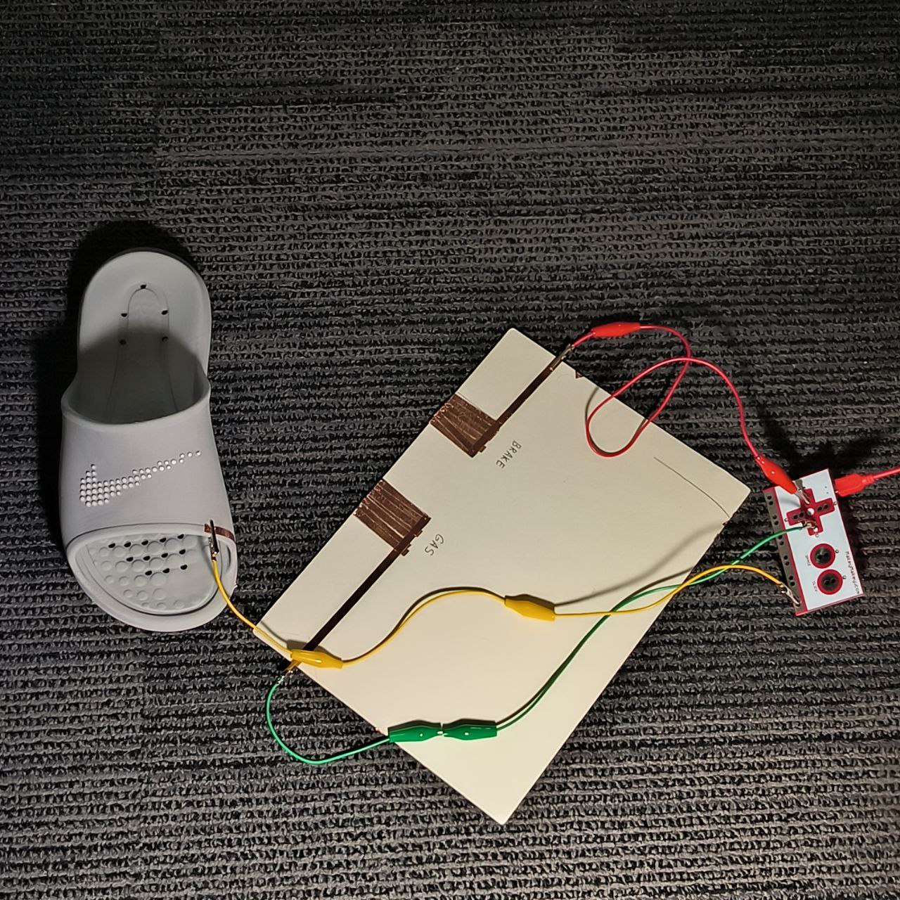 In this wide shot, the full Makey Makey circuit is connected: wires link the slipper to the copper zones and back into the board. The slipper is positioned nearby but not yet activating anything—ready to interact.