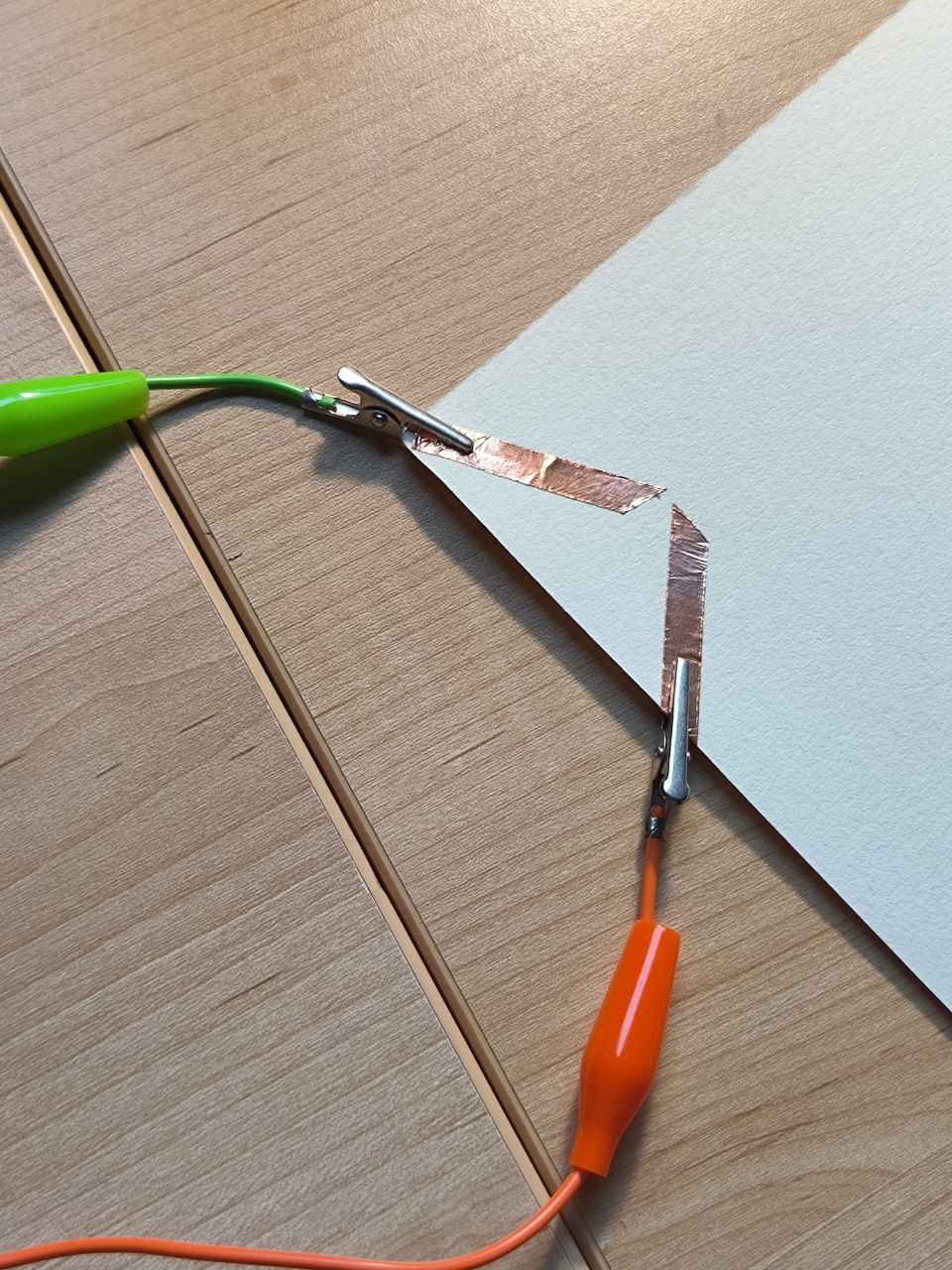 The alligator clips are connected from the Makey Makey directly to the copper tape on the cardstock. This step checks for proper conductivity and confirms that touch will register as a keyboard input.